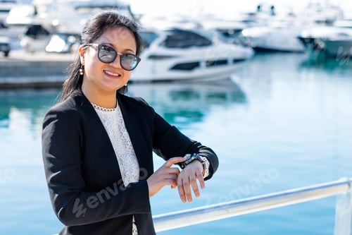 Preview: Asian businesswoman with luxury boats in the background pointing at the clock.