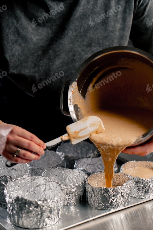 Preview: close up hands female baker in a professional kitchen pours dough into layers of cake molds