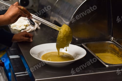 Preview: Restaurant kitchen employee pouring soup into a bowl