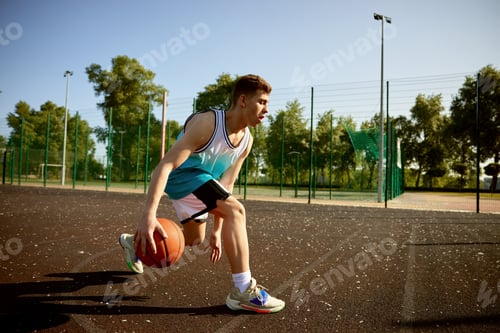 Preview: Young teenager boy training on street court playing basketball