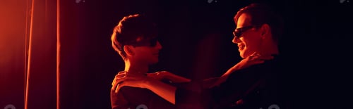 Preview: Side view of smiling and fashionable nonbinary friends in sunglasses hugging each other