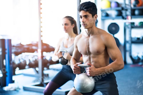 Preview: Young fit couple in gym exercising with kettlebell.