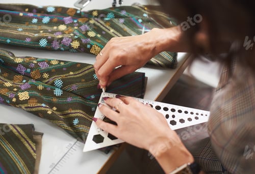 Preview: Tailor workplace: female hands making markings on garment details before sewing on sewing machine.