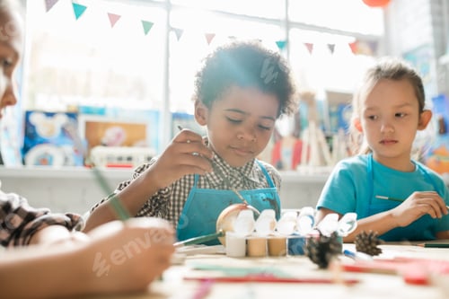 Preview: Serious schoolboy and his classmate painting Christmas decorations by desk