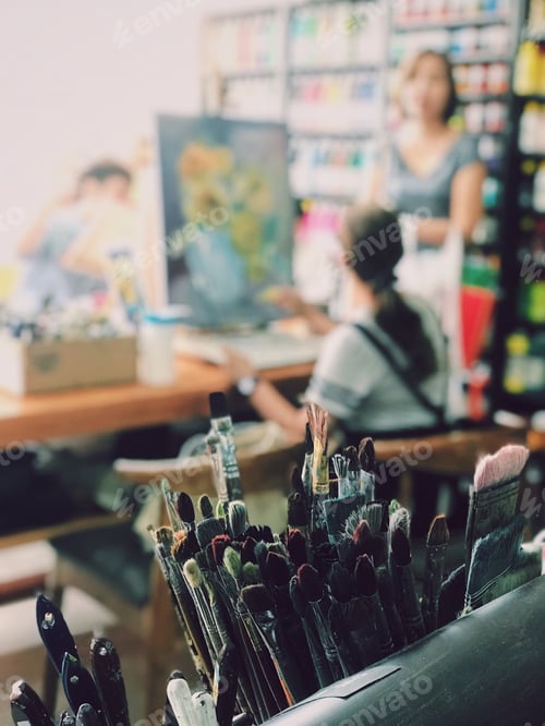 Preview: Set of paint brushes with painter in the background at art studio