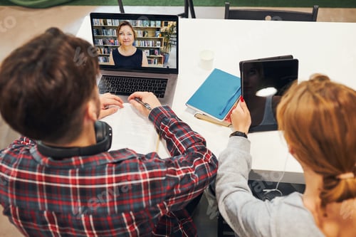 Preview: Students learning in university library. Young man having video class on laptop