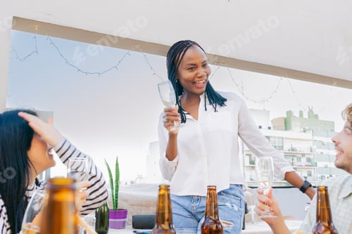 Preview: Black woman happy gathered with friends, toasting on an terrace