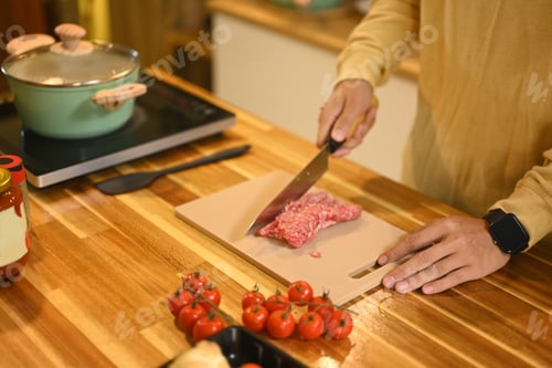 Preview: Young man chopping meat on kitchen counter with fresh ingredients