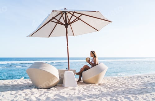 Preview: Beautiful woman in white bikini resting at sundeck seashore of Maldive island - drinking coconut bev