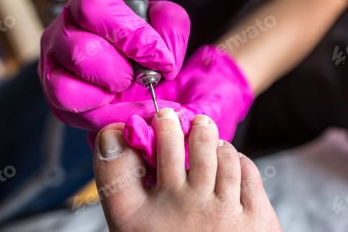 Preview: Pedicurist master in pink gloves cuts the cuticle and shellac toe nails in the pedicure salon