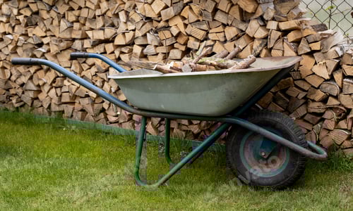 Preview: chopped firewood in a woodpile in the country and a wheelbarrow with firewood