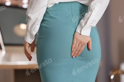 Preview: Young woman suffering from hemorrhoid in office, closeup