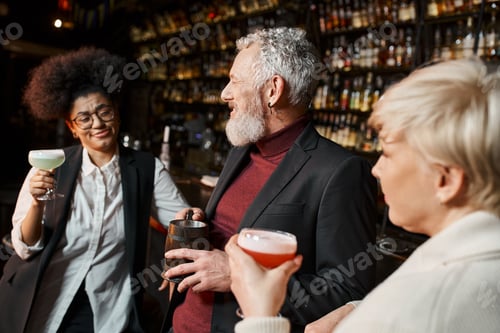 Preview: bearded middle aged man smiling near multiethnic women with cocktails, colleagues resting in bar