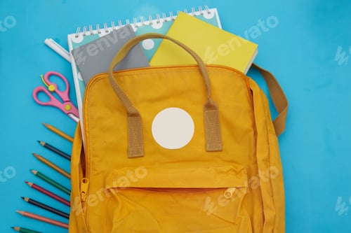 Preview: Backpack on the table with notepads, scissors, colored pencils on a blue background