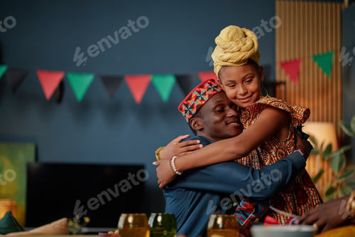 Preview: Young Black Man Hugging Young Black Girl during Kwanzaa Celebration Indoors
