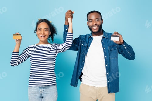Preview: happy african american couple holding hands while showing credit cards on blue