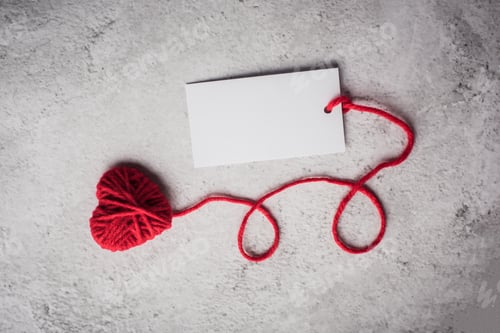 Preview: Red yarn heart shaped with white note card on the wall background