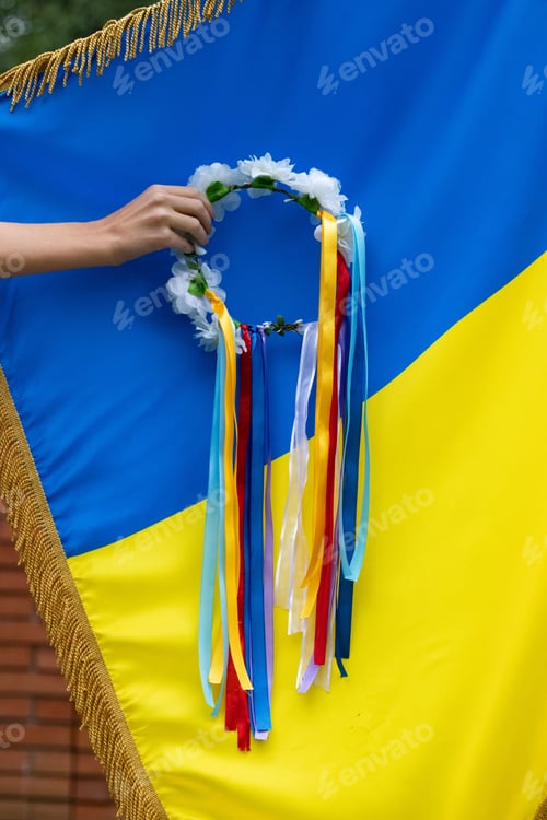 Preview: Vertical shot of a hand holding a flower crown against the Ukrainian flag