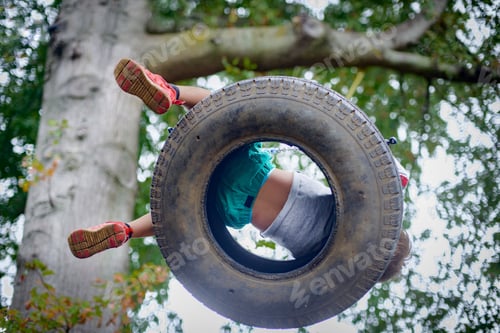 Preview: Low angle view of boy playing on tyre swing in garden