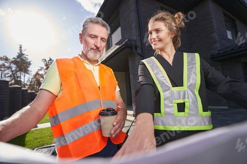 Preview: Satisfied construction engineer pointing out something on drawings to worker