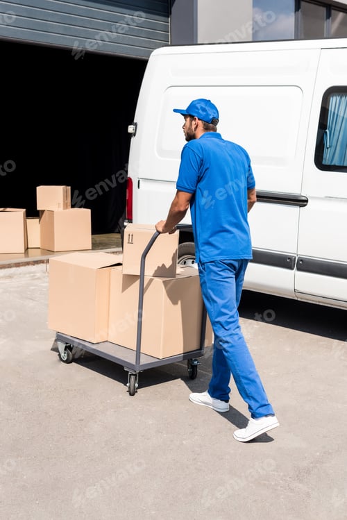 Preview: delivery man driving cart with cardboard boxes into warehouse