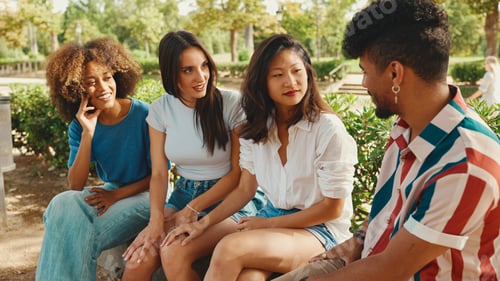 Preview: Group of friends talking, using cellphone while relaxing in the park at picnic
