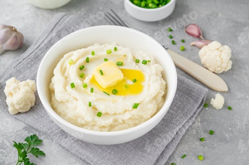 Preview: Cauliflower puree with butter and green onions in a white bowl. Healthy food. Copy space.