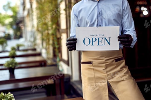 Preview: Unrecognizable waiter holding open sign at pub's doorway.