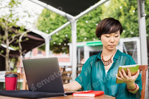 Preview: Woman sitting with a laptop at table in a cafe, with digital tablet.