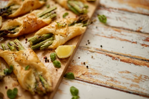 Preview: Baked green asparagus wrapped in puff pastry. Served on wooden board. With copy space
