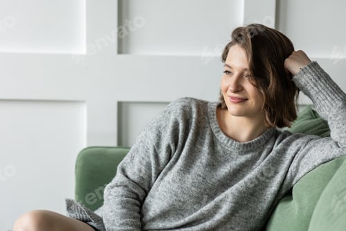 Preview: Young brunette woman at home sitting on the green sofa. Feeling relaxed and happy. Portrait