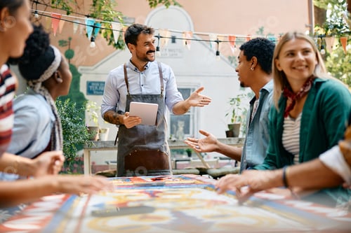 Preview: Happy waiter talking to group of guests in a cafe.