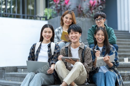 Preview: Group of happy young Asian students in casual clothes sitting on the front steps of a university bui