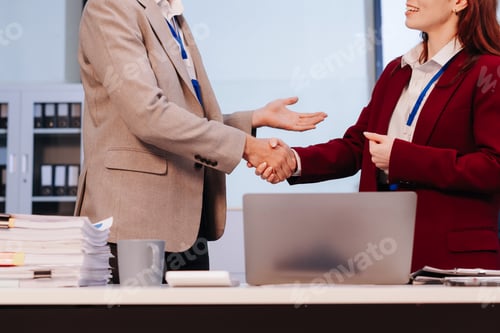 Preview: Happy businessman and businesswoman shaking hands at group board meeting.