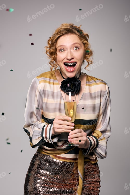 Preview: Joyful young woman celebrating with a glass of champagne amid festive confetti at a party