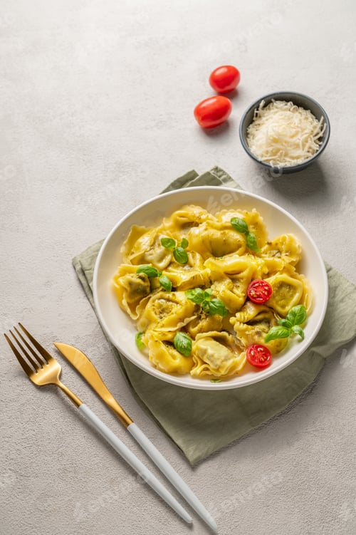 Preview: Tortellini pasta with parmesan, pesto and basil in a plate on a light background with tomato
