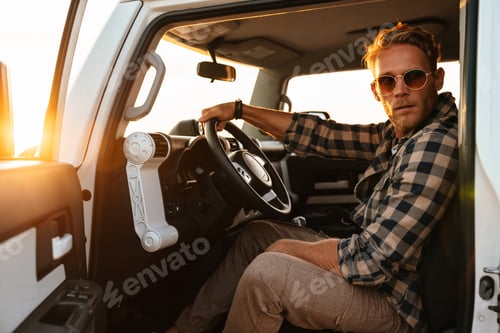 Preview: Attractive young man sitting on a front sit in hos car at the beach, open door