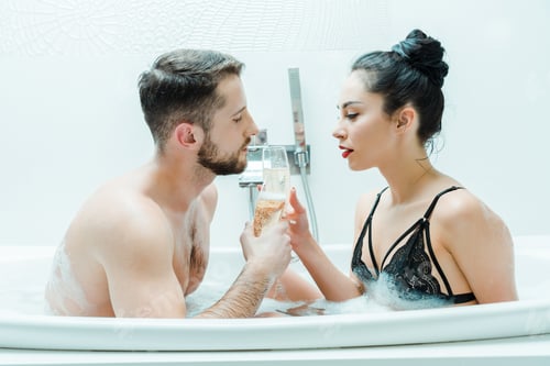 Preview: handsome man and sexy young woman holding champagne glasses in bathtub