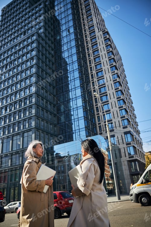 Preview: Two stylish women with laptops standing on the street