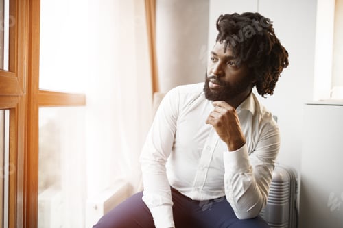 Preview: Black man businessman sitting and looking at window in hotel room