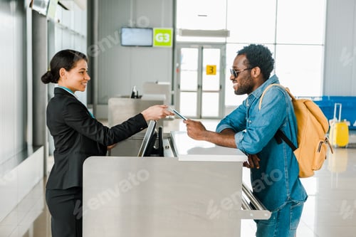 Preview: smiling african american airport worker taking passport and air ticket from tourist with backpack