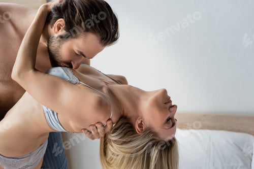Preview: side view of brunette man kissing breast of passionate blonde woman in underwear
