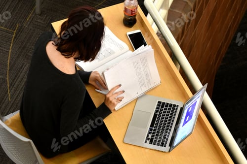 Preview: Female student Studying her notes with laptop computer overhead view