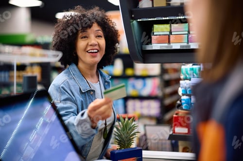 Preview: Happy mature woman paying with credit card in a supermarket.