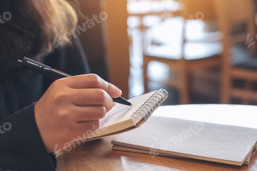 Preview: Closeup image of a hand holding and writing on blank notebook on table in cafe