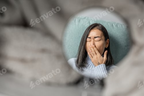 Preview: a young pretty brunette of Asian appearance in a pale blue sweater yawns with her hand over her mout