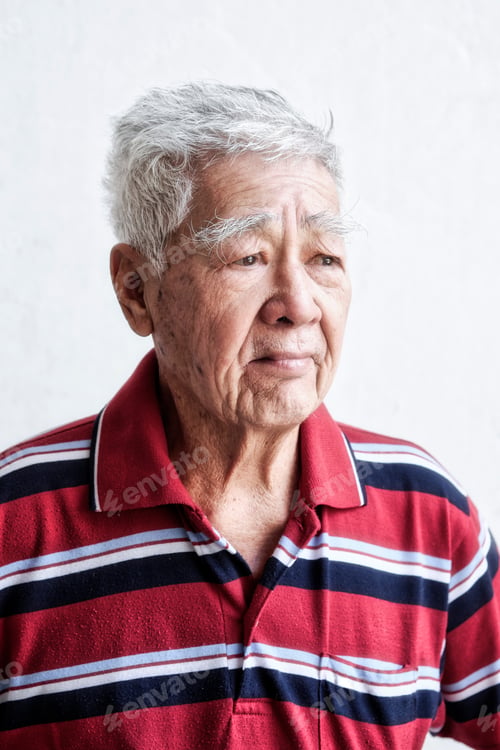 Preview: Portrait of an elderly Asian man in deep thought. Standing against white wall.