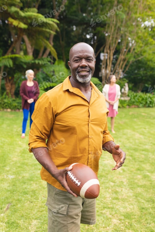 Preview: Portrait of african american senior man playing rugby with friends in backyard