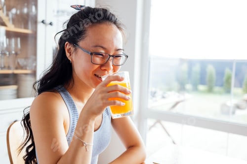 Preview: A smiling attractive Asian woman drinks freshly squeezed orange juice