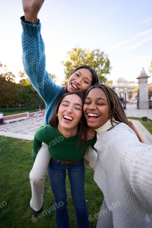 Preview: Happy photo of three diverse female friends taking cheerful selfie doing piggyback. Girls having fun